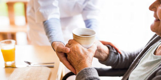 enfermera lleva una bebida a un anciano